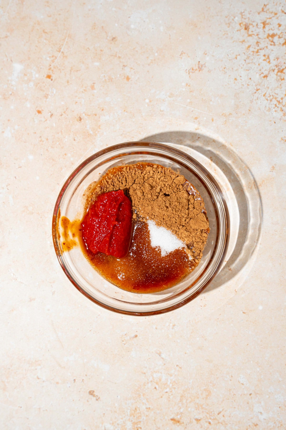 A blender jar with ingredients to make Tex Mex paste including adobo sauce, tomato paste, cocoa powder, and sugar. The jar is on a tan counter.
