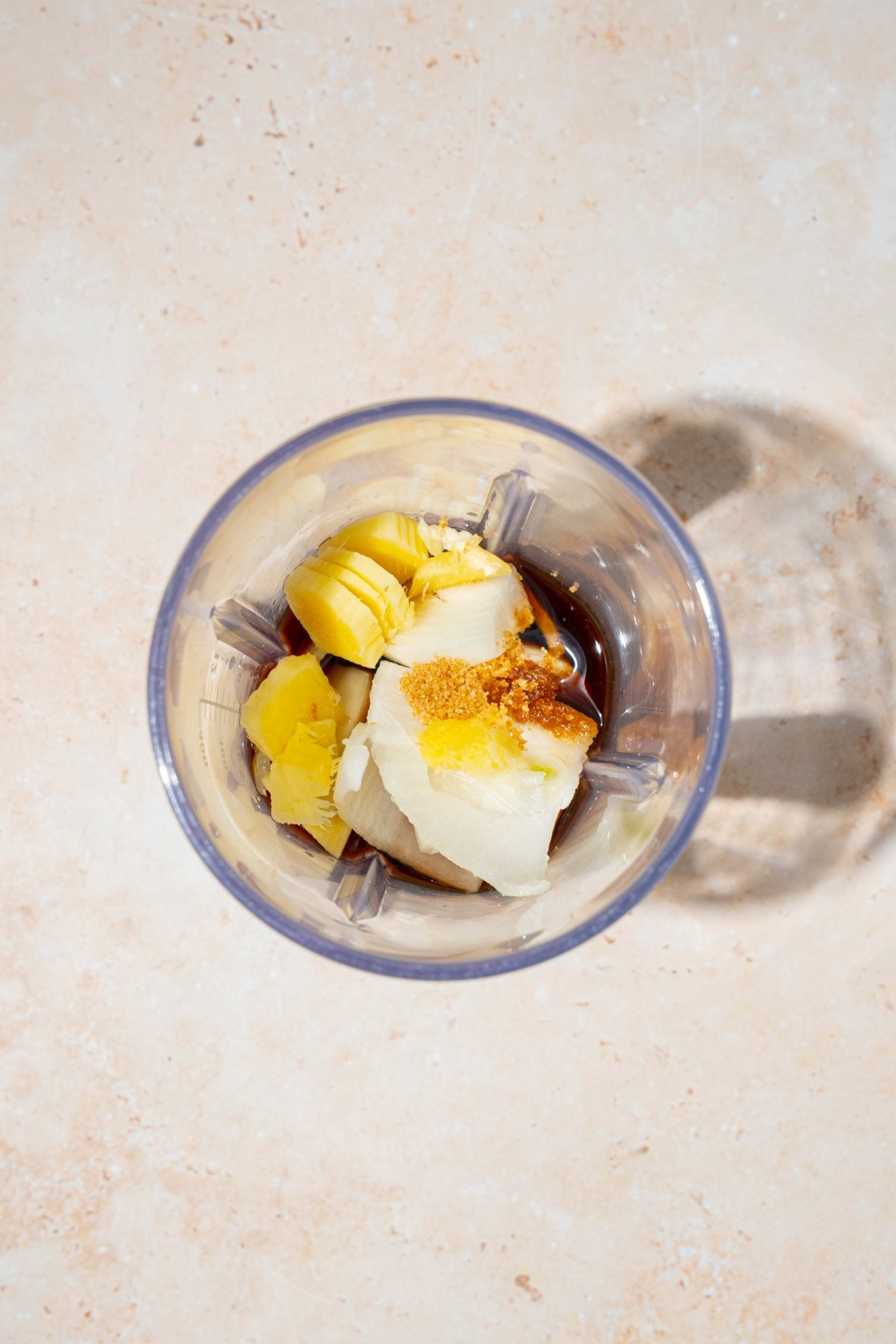 A blender jar with ingredients to make hibachi ginger sauce including tamari, yellow onion, ginger, lemon, rice vinegar, and brown sugar. The jar is on a tan counter.