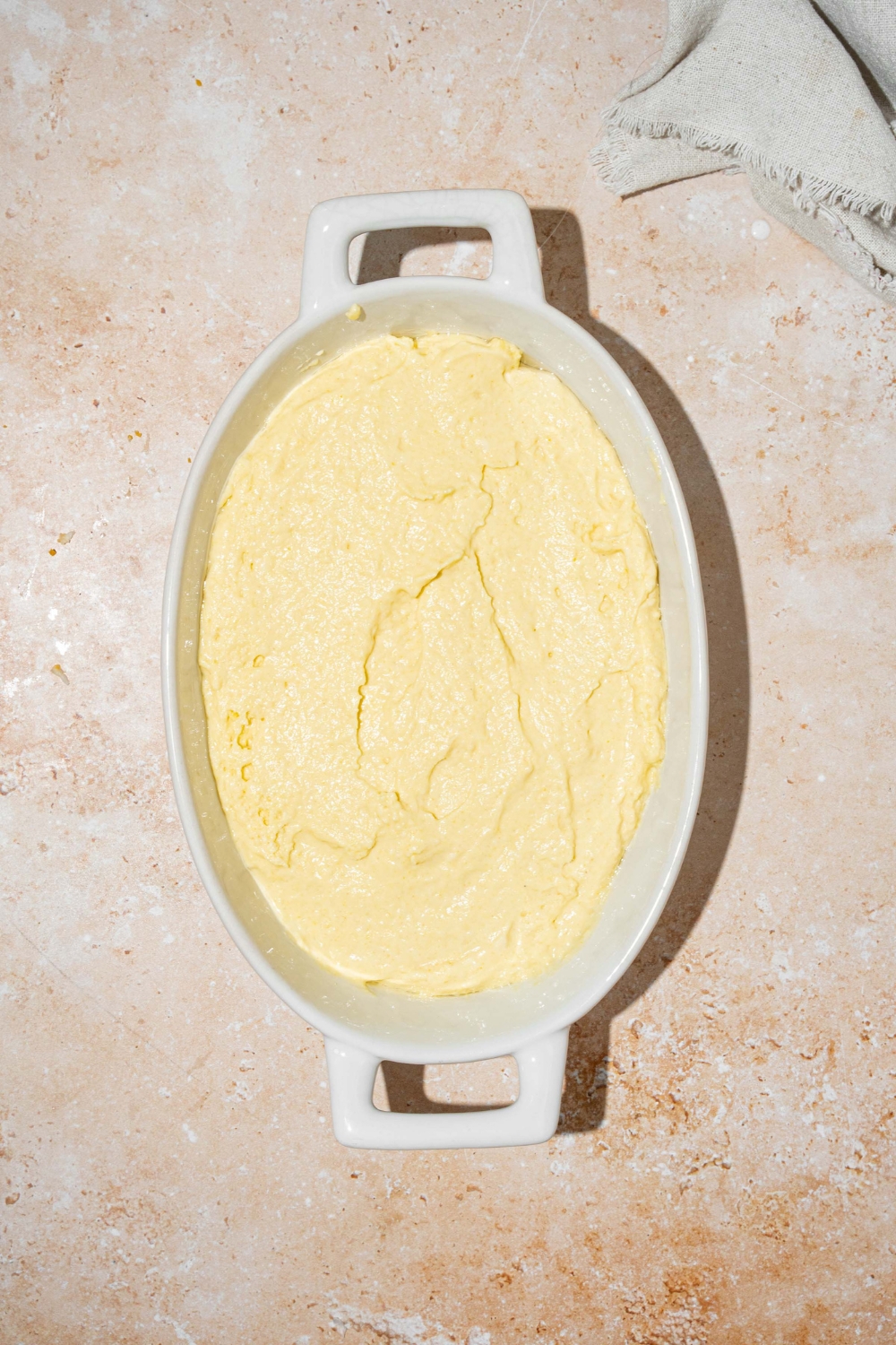 An oval baking dish with cornbread dough mixture. The dish is on a tan counter.