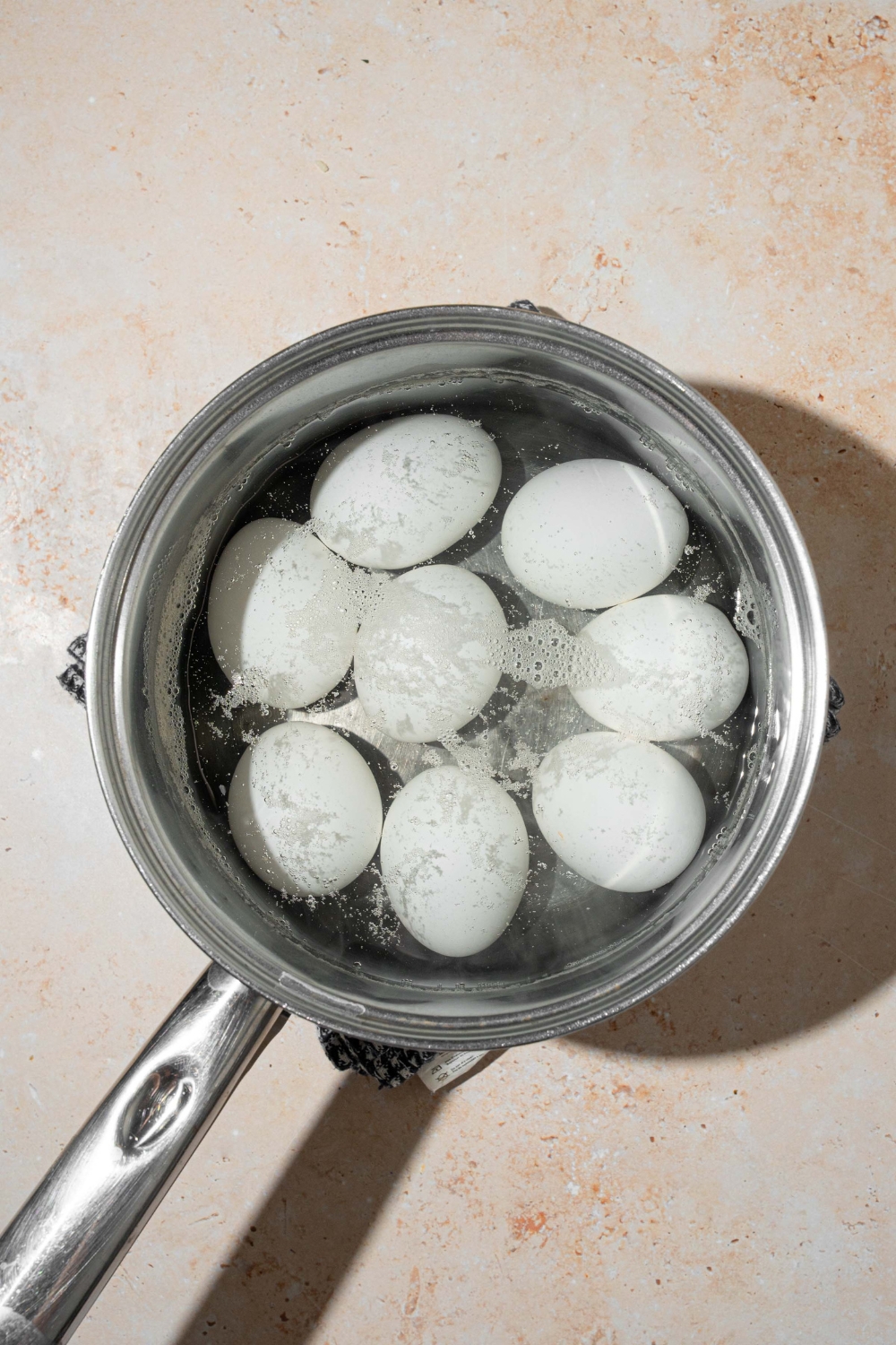 A pot with eggs boiling in water. The pot is on a tan counter.