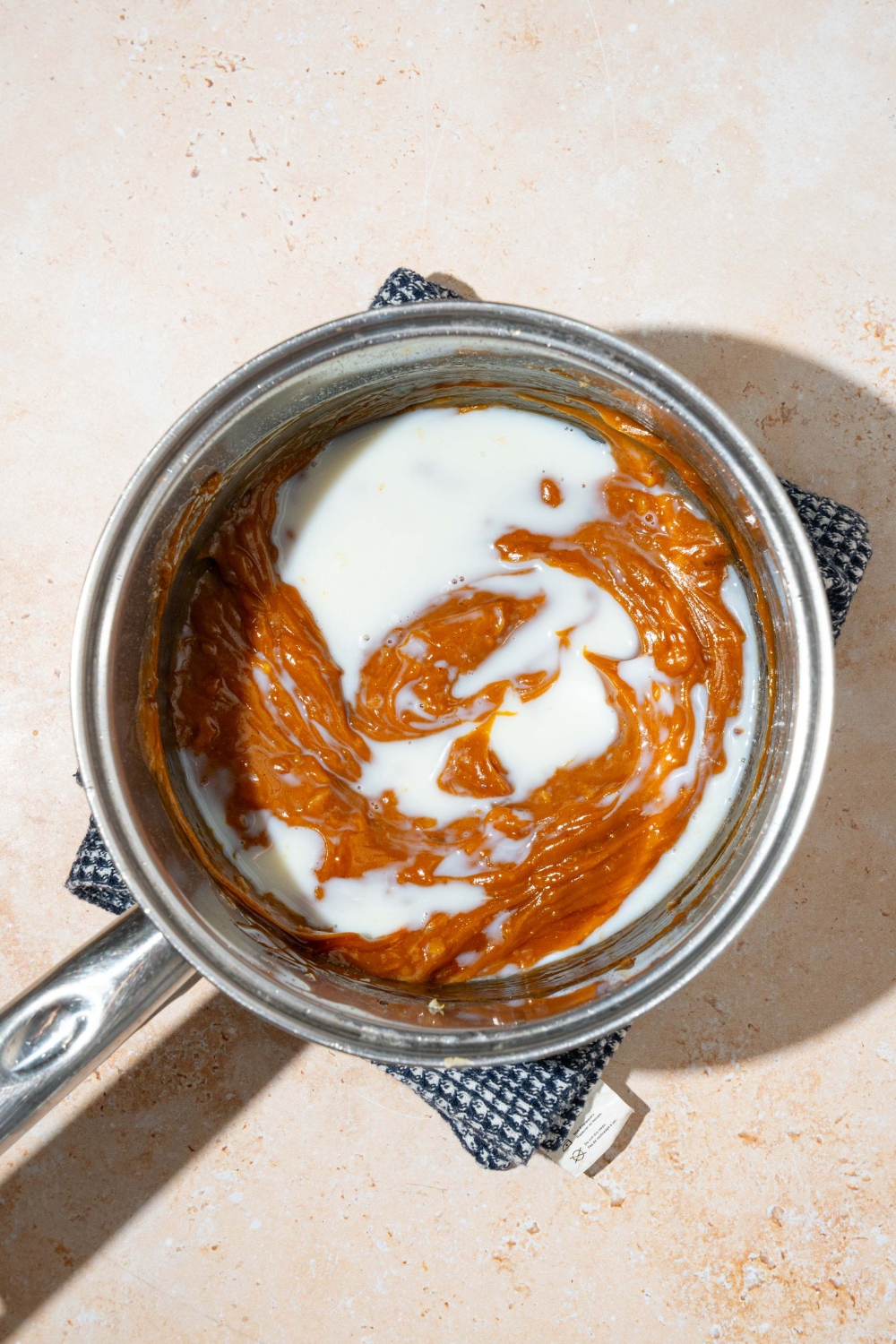 A pot with a peanut sauce mixture with milk. The pot is on a tan counter with a dish towel.