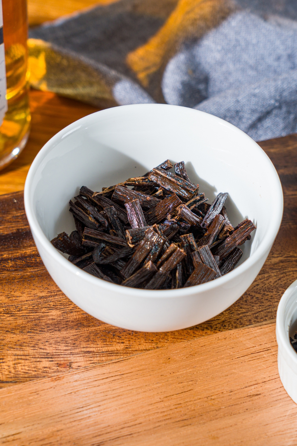 A white bowl with chopped vanilla bean pods with the seeds removed. The bowl is on a wooden counter with a blue cloth napkin.