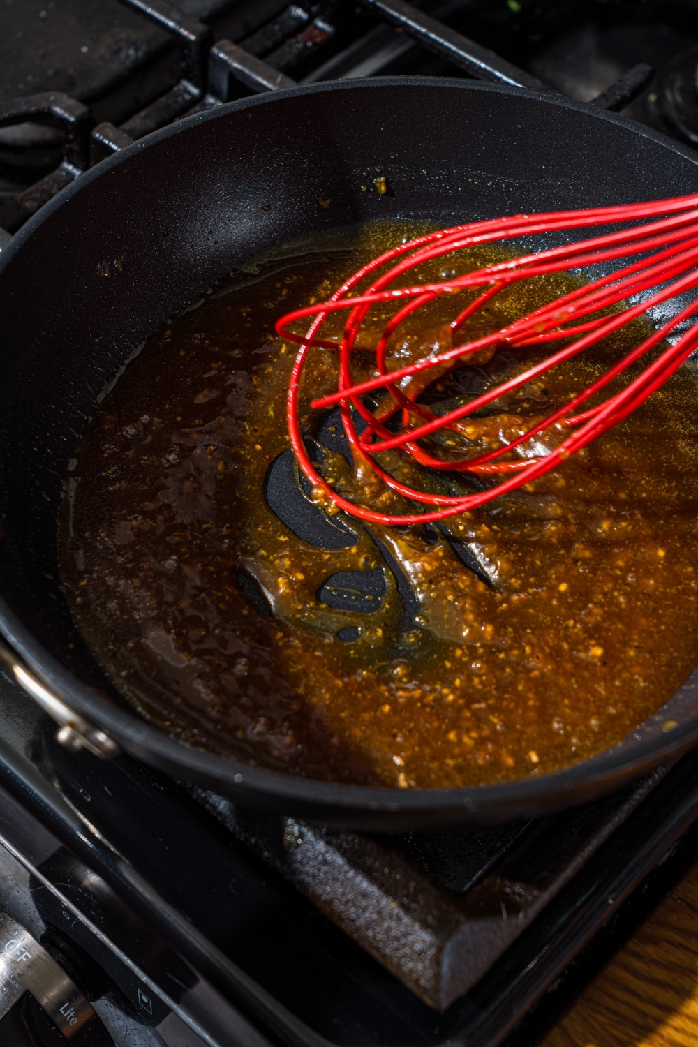 A skillet with a whisk mixing honey lemon pepper sauce as it cooks on the stove.