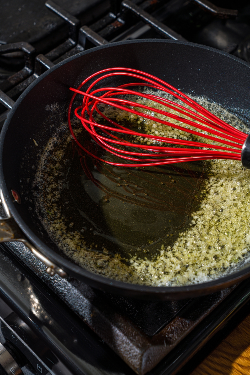 A skillet with a whisk mixing butter and garlic as it cooks on the stove.