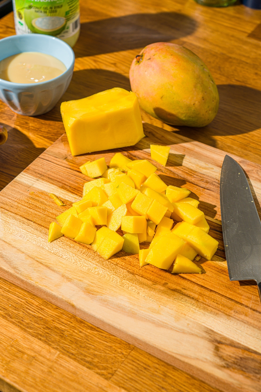 A wooden counter with a knife and diced mango. The board is on a wooden counter.