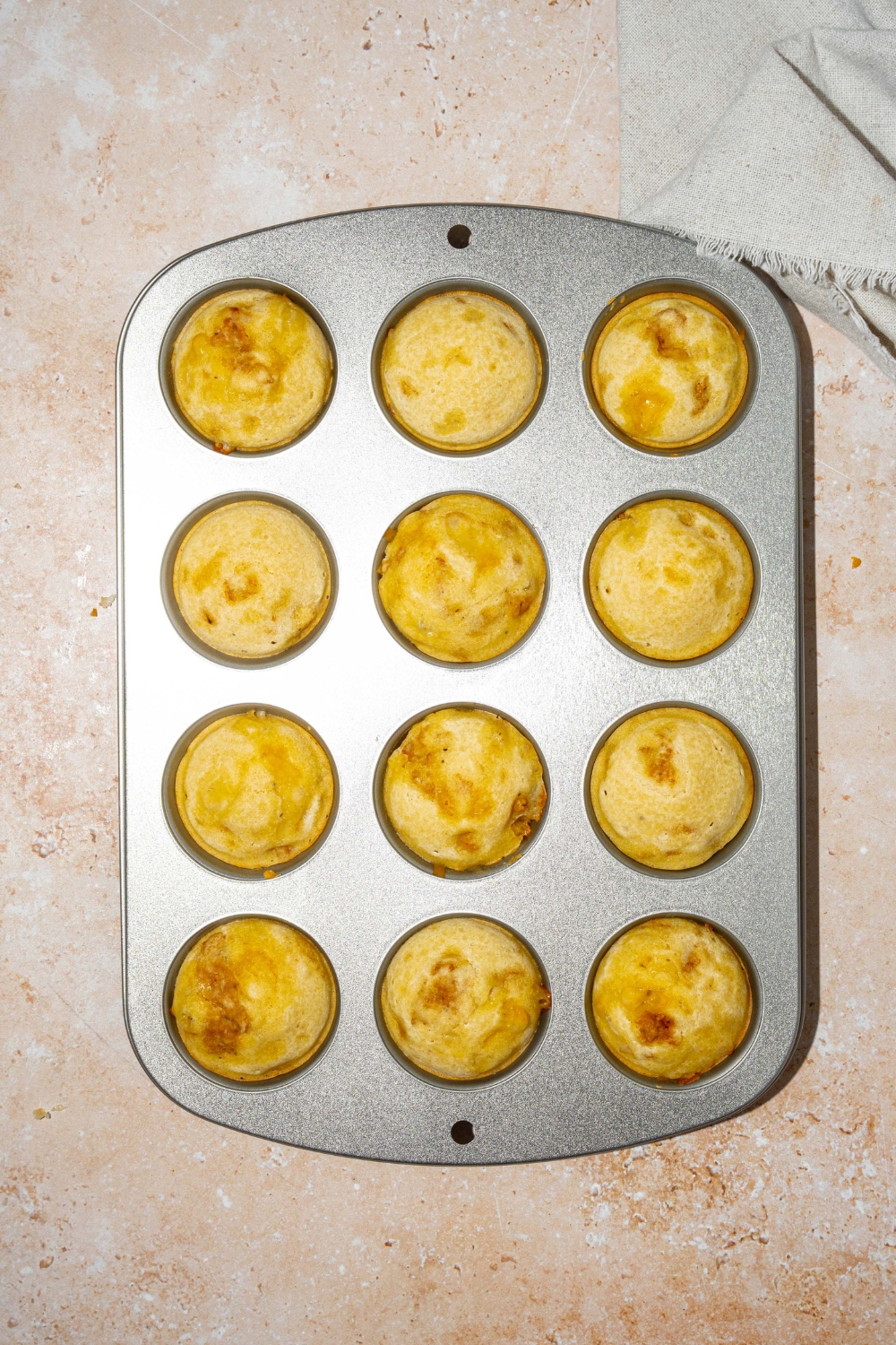 A mini muffin tin with baked pancake sausage muffins. The tin is on a tan counter.
