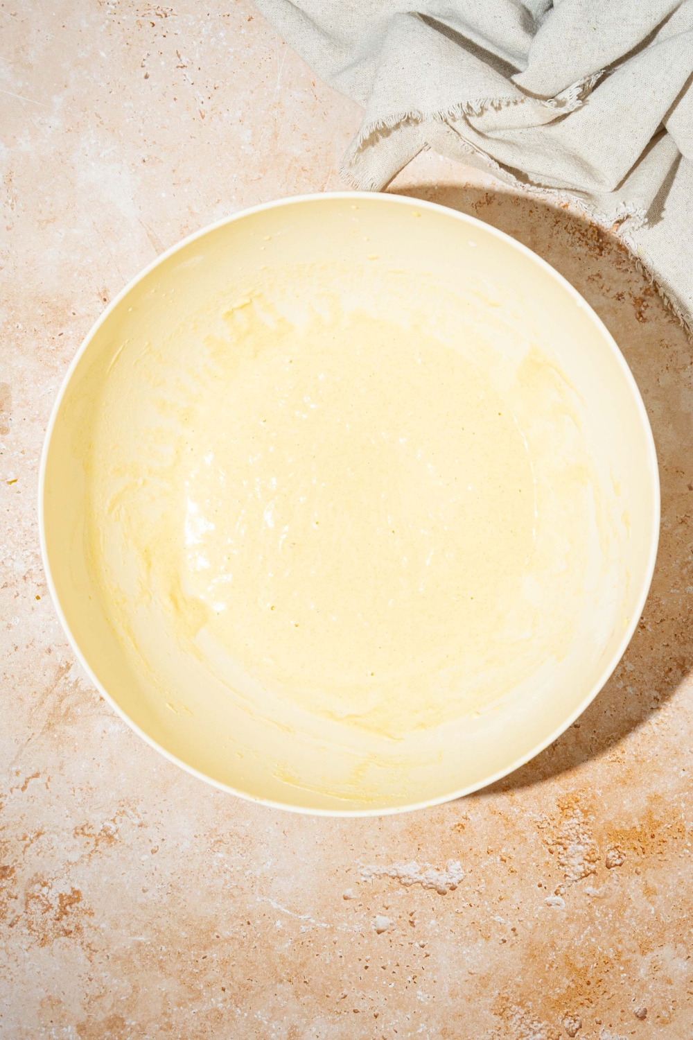 A large white bowl with pancake batter. The bowl is on a tan counter.