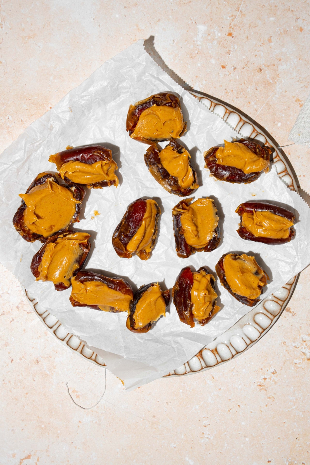 A white plate lined with parchment paper with dates stuffed with peanut butter. The plate is on a tan counter.