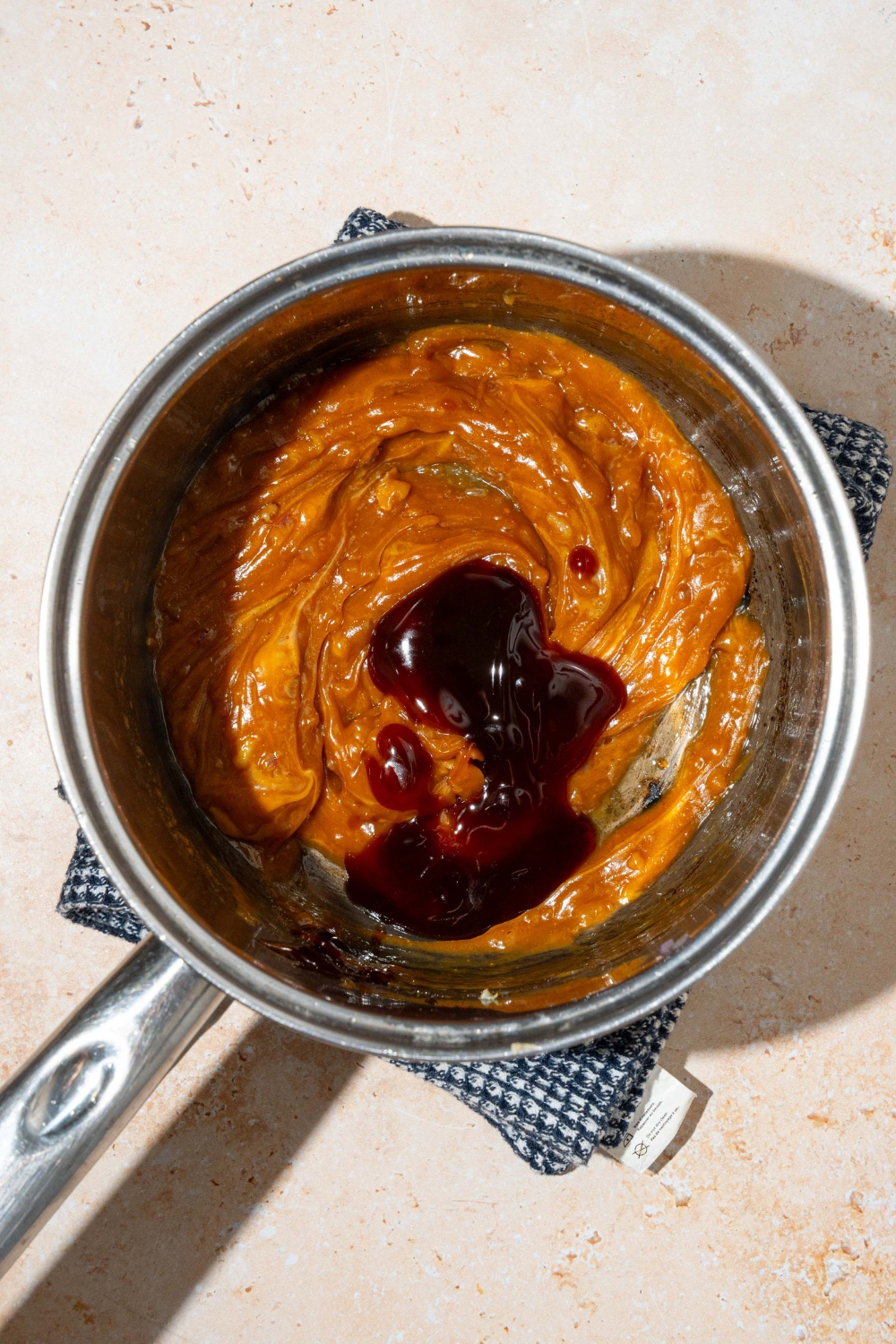 A pot with a peanut sauce mixture with hoisin. The pot is on a tan counter with a dish towel.