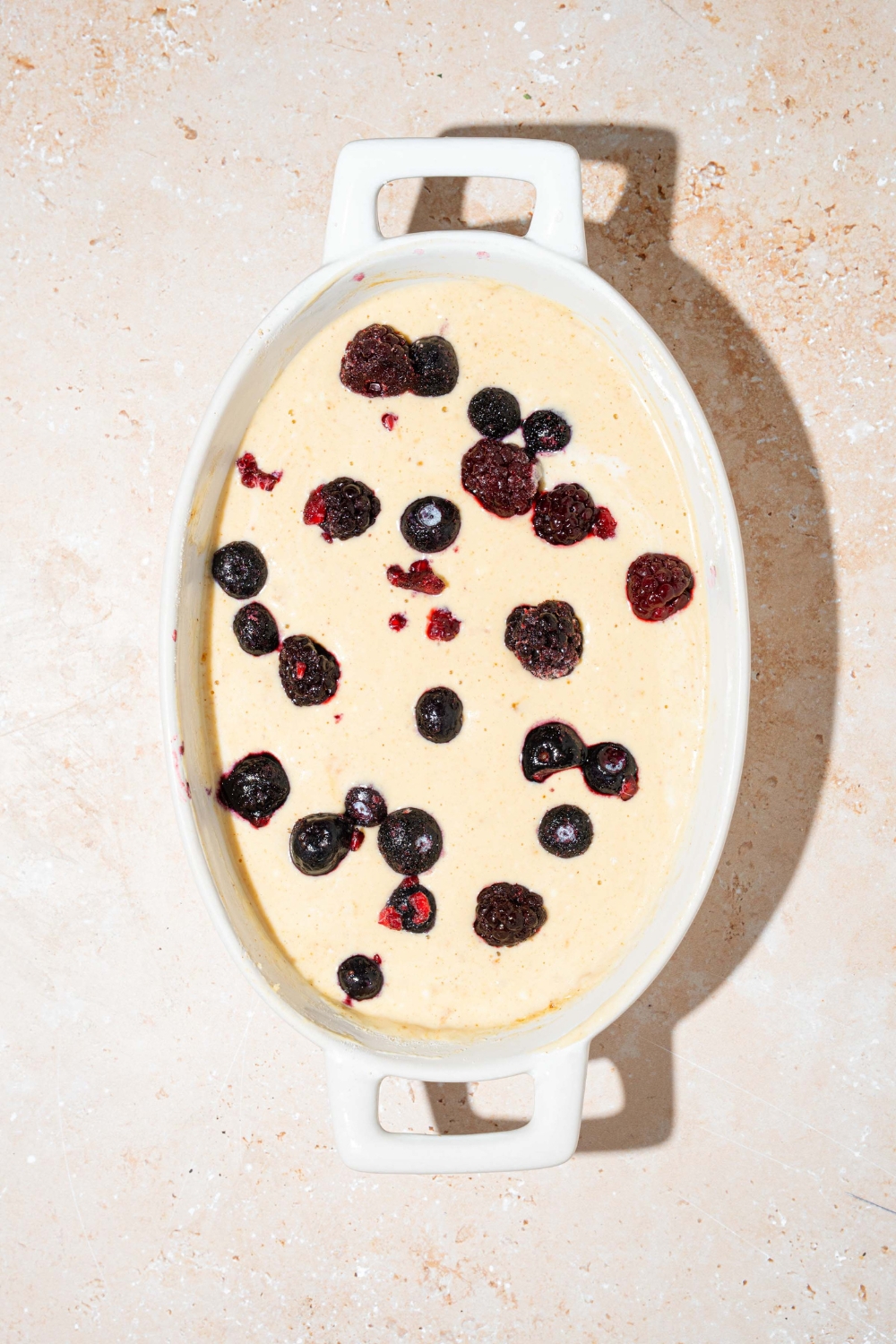 An oven safe bowl with protein pancake batter with blueberries on top. The bowl is on a tan counter.