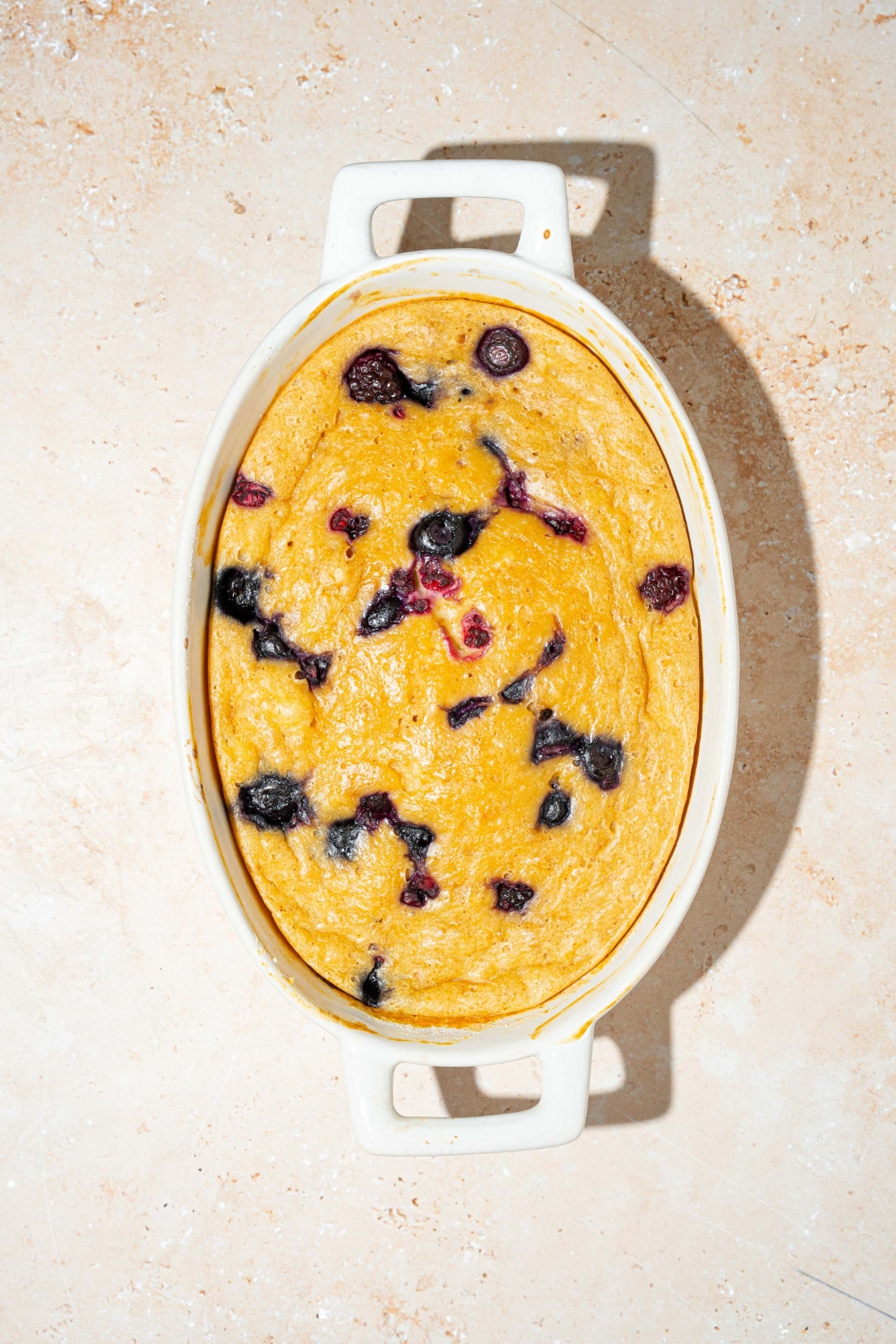 An oven safe bowl with baked protein pancake with blueberries. The bowl is on a tan counter.