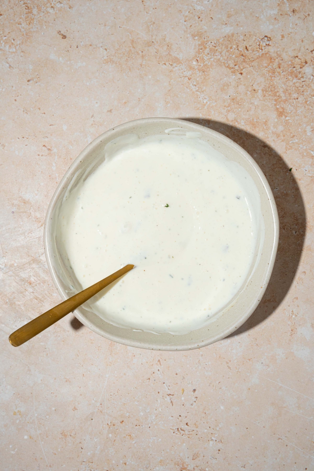 A white bowl with a spoon mixing cottage cheese ranch dip. The bowl is on a tan counter.