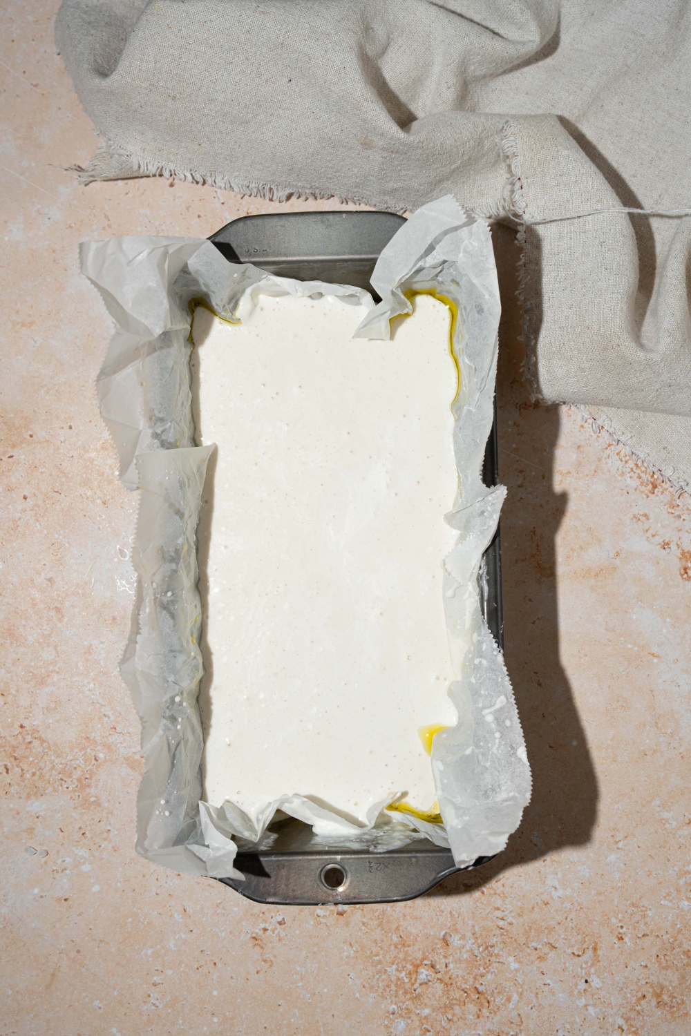 A loaf pan lined with parchment paper with rice blender bread dough. The pan is on a tan counter.