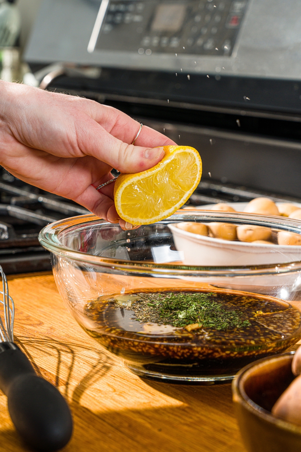 A lemon being squeezed into a glass bowl of steak kabob marinade. The bowl is on a wooden counter.