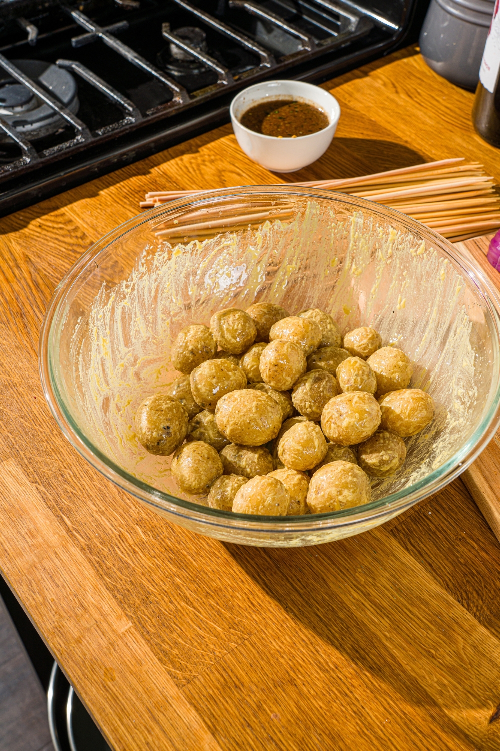 A large glass bowl with cooked potatoes tossed in a mustard dressing. The bowl is on a wooden counter.