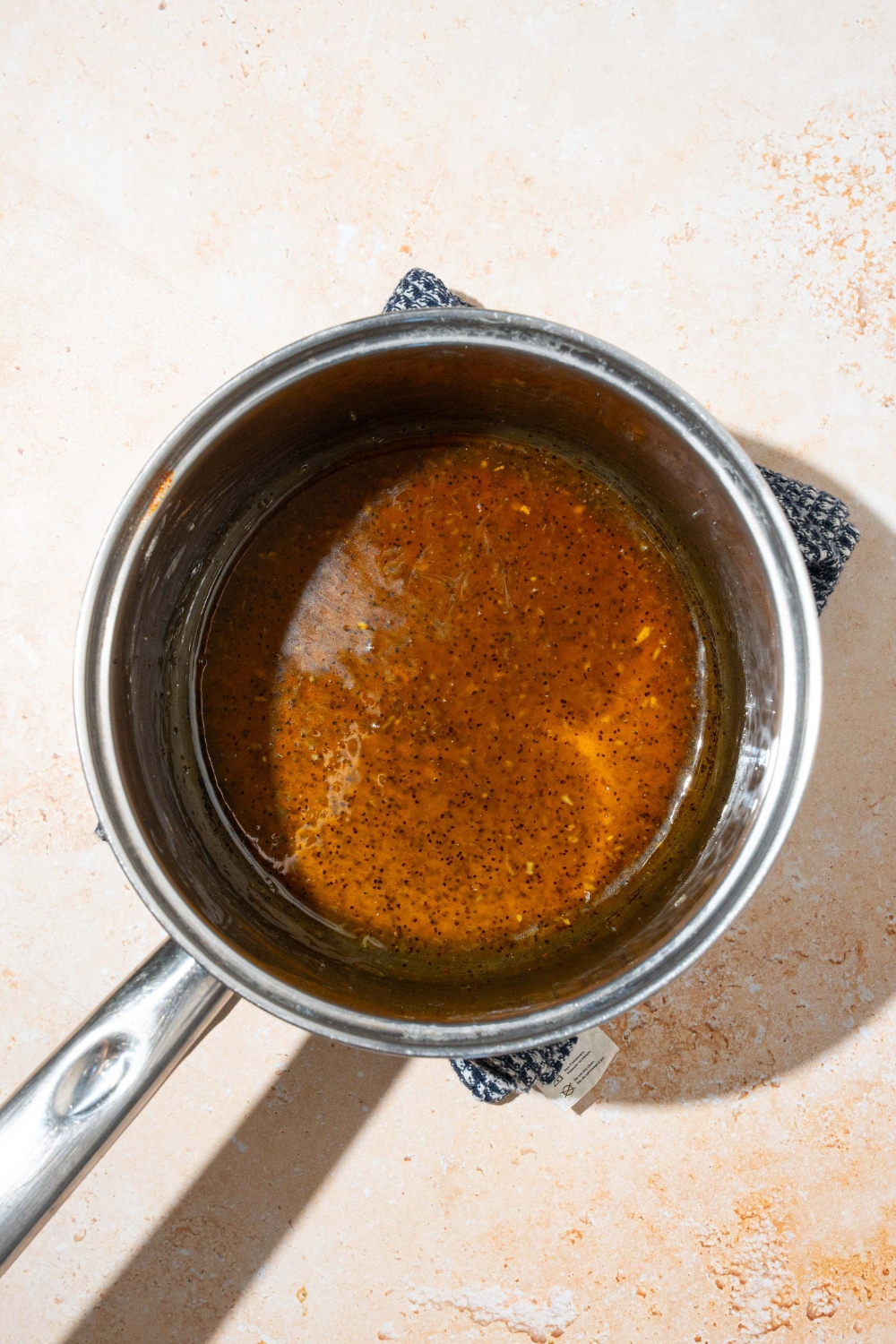 A saucepan with cooked sweet onion sauce. The saucepan is on a tan counter with a dish towel.