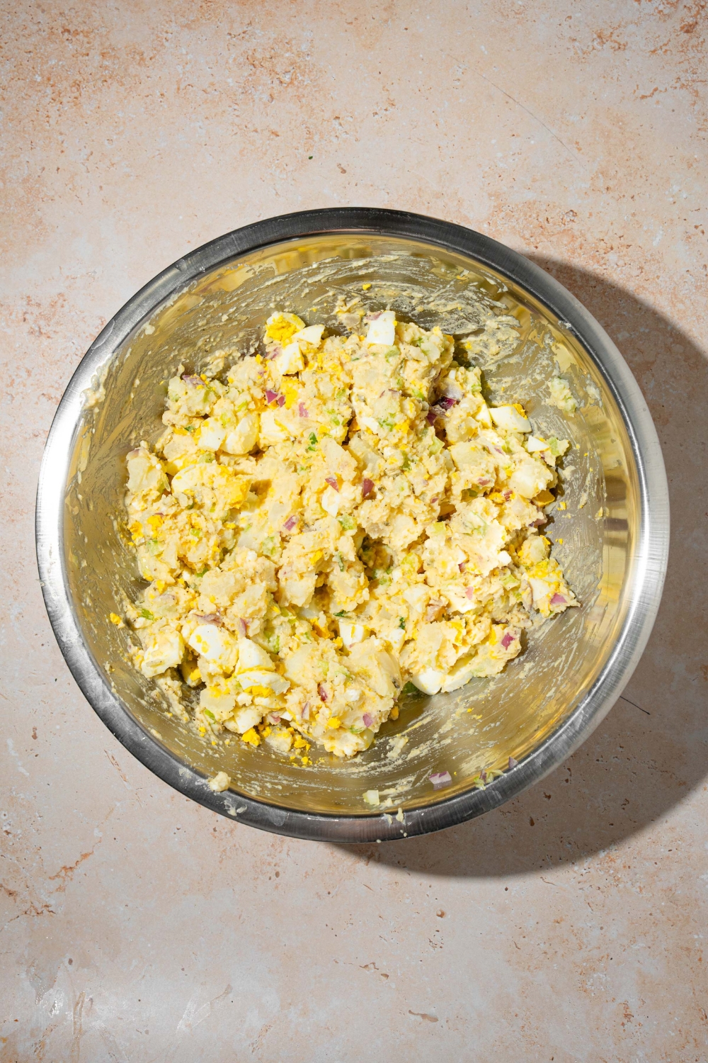 A large bowl with deviled egg potato salad tossed in dressing. The bowl is on a tan counter.
