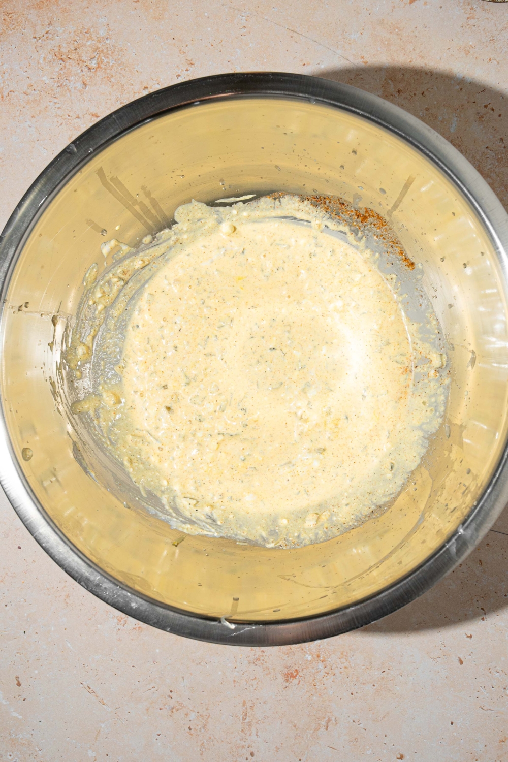 A large mixing bowl with potato salad dressing. The bowl is on a tan counter.