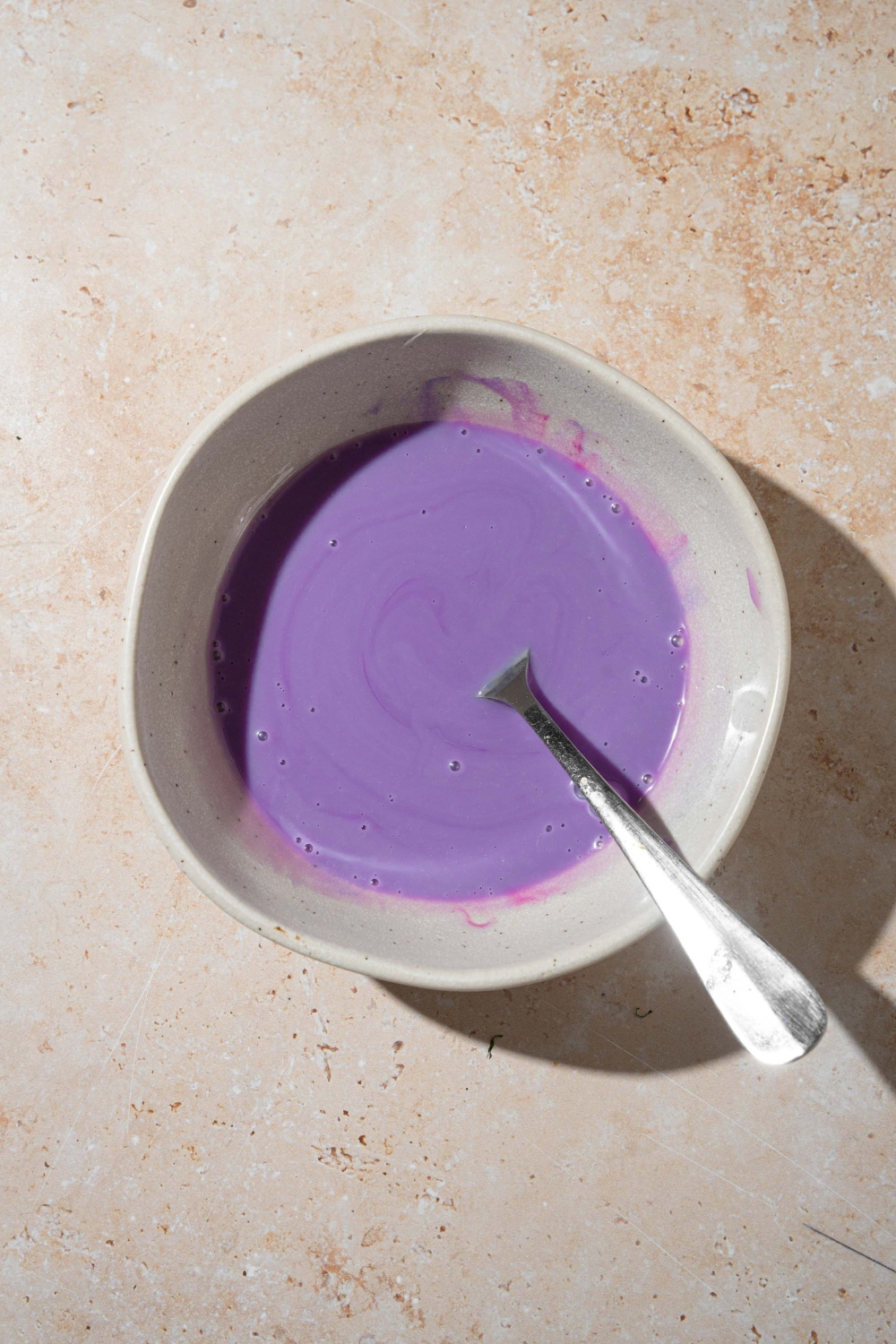 A white bowl with a fork dipped in a ube sauce mixture. The bowl is on a tan counter.