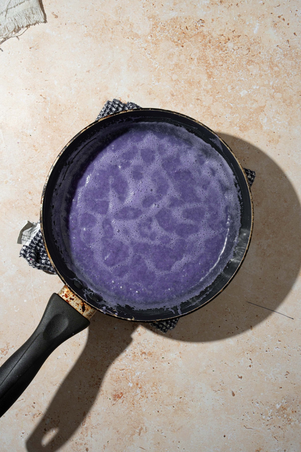 A skillet with a cooked ube sauce. The skillet is on a tan counter.