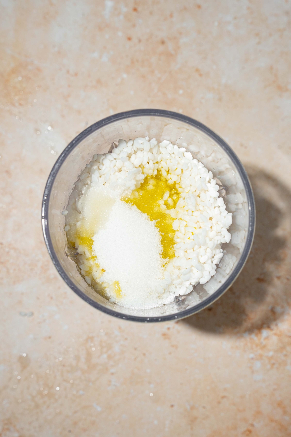 A large bowl with ingredients to make rice blender bread including soaked rice, oil, honey, water, and yeast. The bowl is on a tan counter.