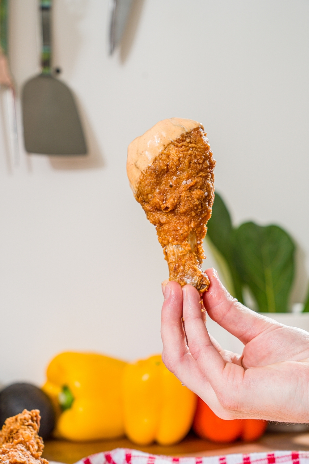 A hand holding a piece of copycat KFC fried chicken dipped in a mayo dipping sauce.