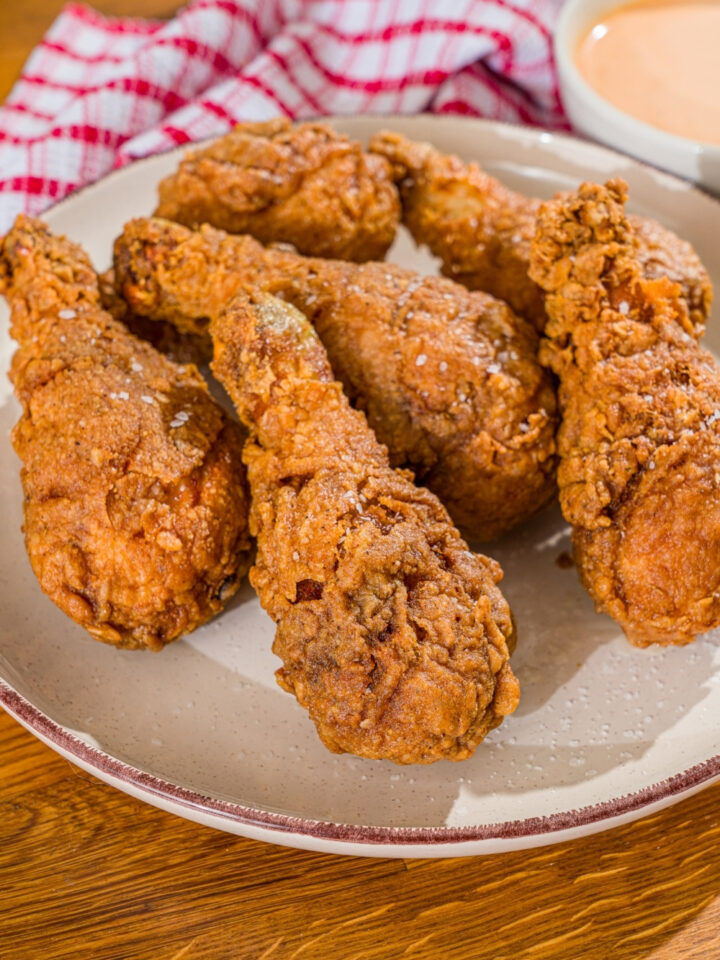 A white plate with copycat KFC original chicken recipe. The plate is on a wooden counter with a red checkered napkin.