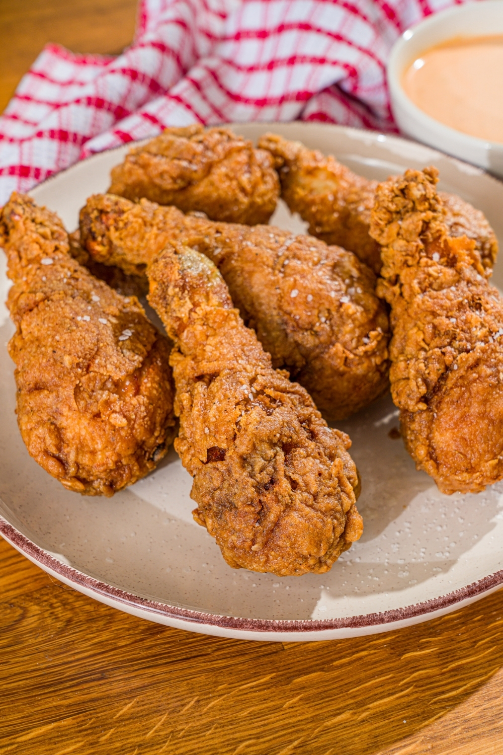 A white plate with copycat KFC original chicken recipe. The plate is on a wooden counter with a red checkered napkin.