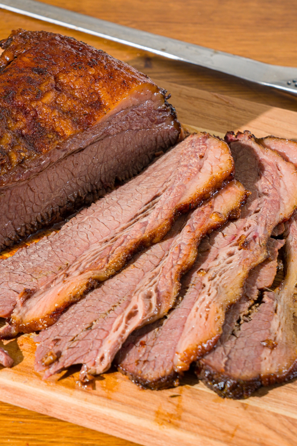 A wooden cutting board with oven baked beef brisket. Some of the brisket has been sliced.