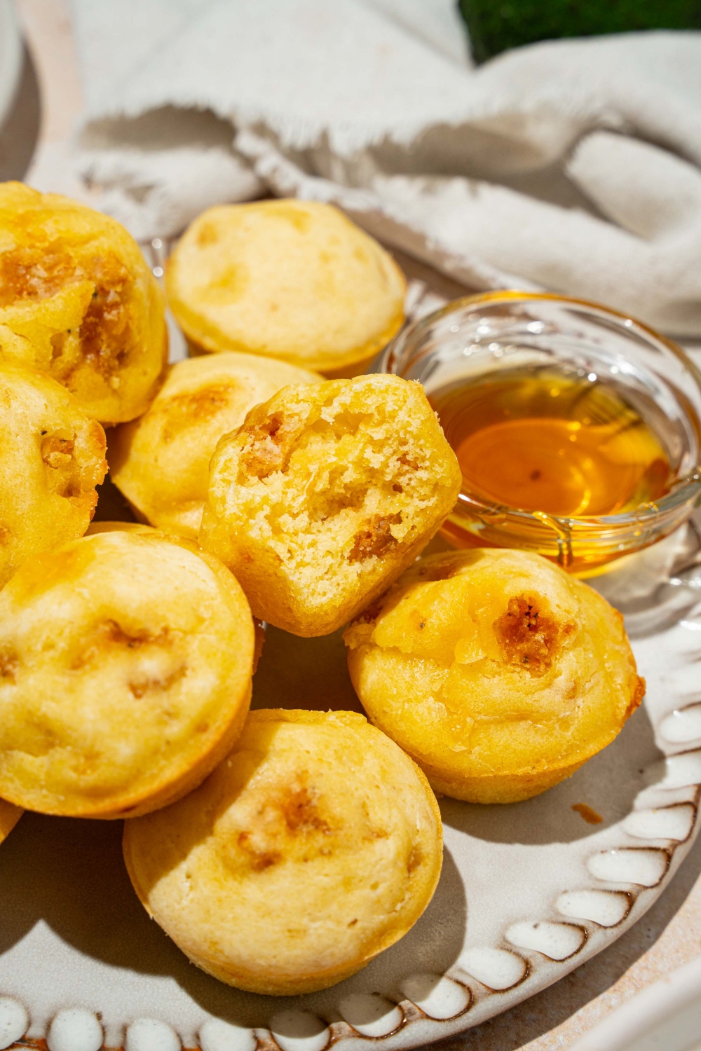 A plate with a pile of pancake sausage muffins and small bowl of syrup. There is a bite taken from one of the muffins. The plate is on a tan counter.