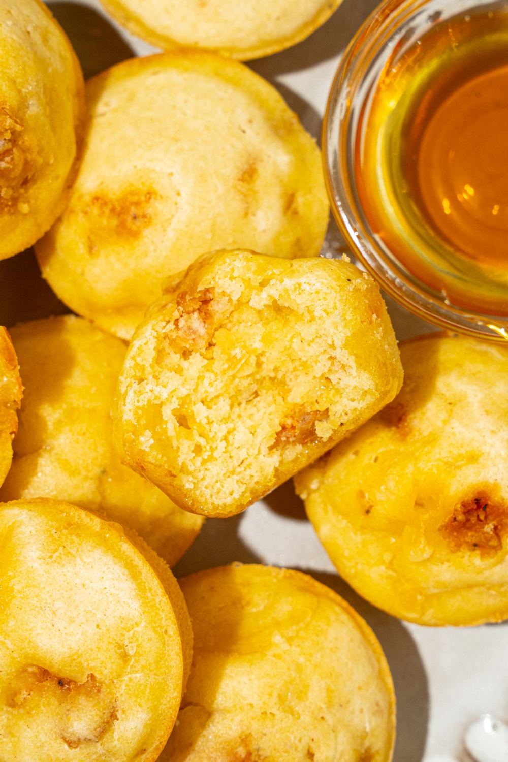 A plate with a pile of pancake sausage muffins and small bowl of syrup. There is a bite taken from one of the muffins.