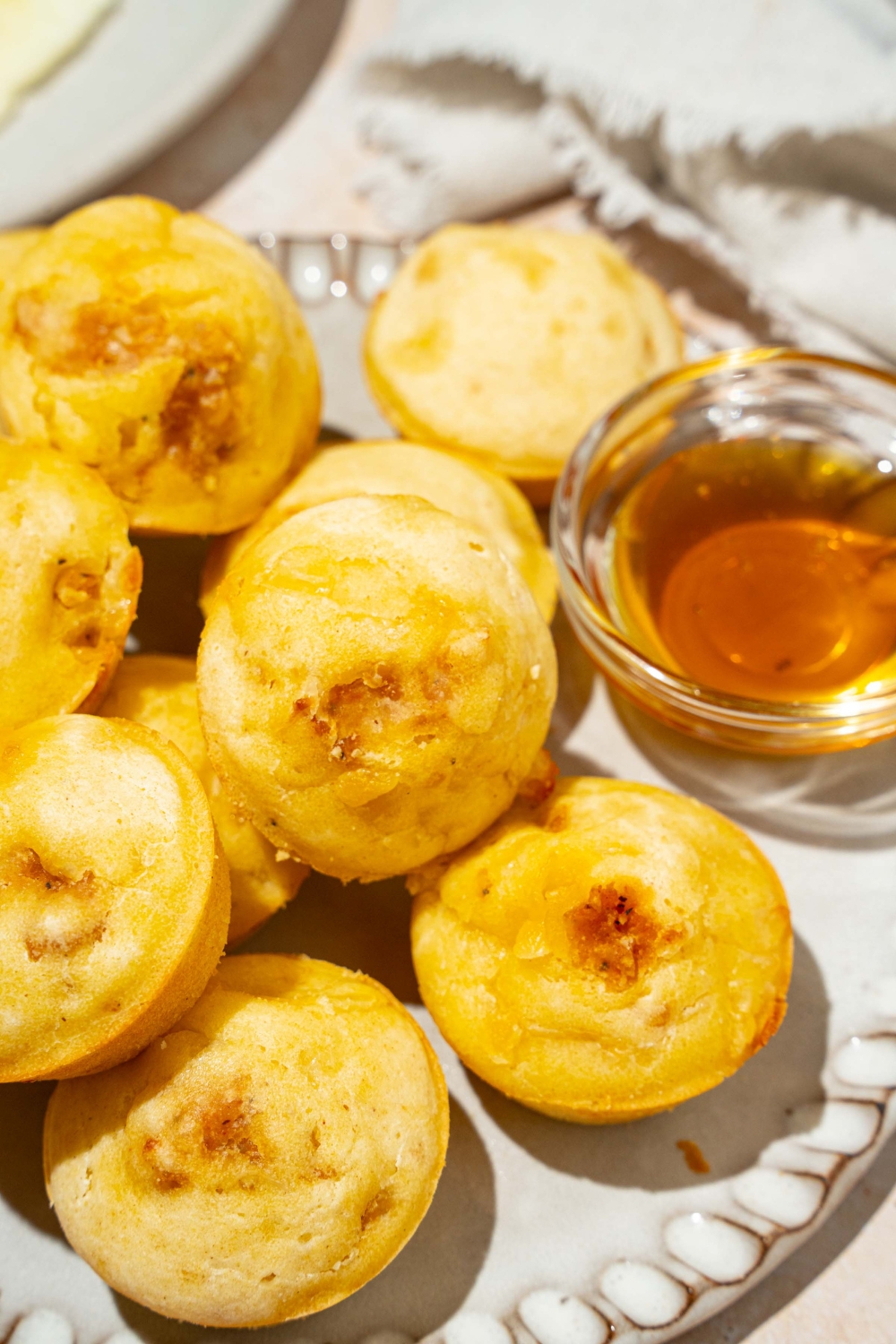 A plate with a pile of pancake sausage muffins and small bowl of syrup. The plate is on a tan counter with a white cloth napkin.