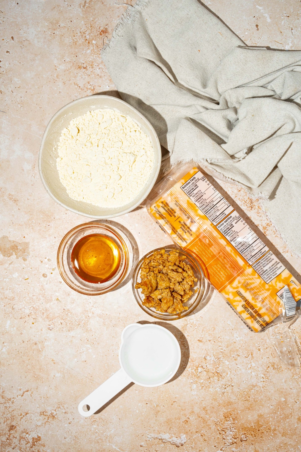 A tan counter with bowls of ingredients to make pancake sausage muffins including pancake mix, water, breakfast sausage, shredded cheese, and syrup.