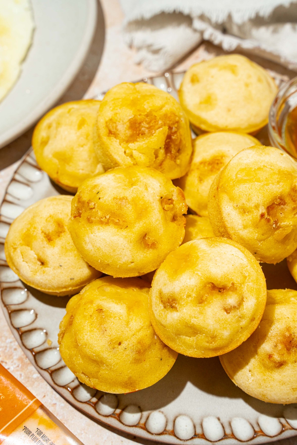 A plate with a pile of pancake sausage muffins. The plate is on a tan counter with a white cloth napkin.