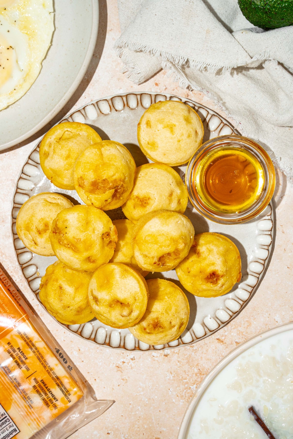 A plate with a pile of pancake sausage muffins and small bowl of syrup. The plate is on a tan counter with a white cloth napkin.