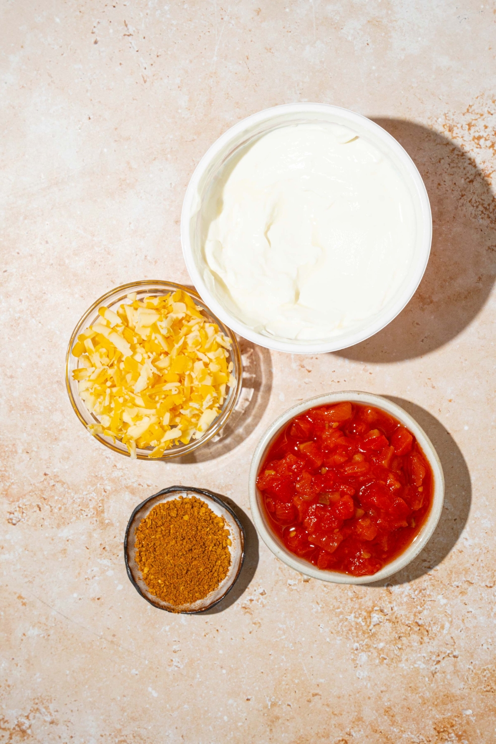 A tan counter with small bowls of ingredients to make poolside dip including sour cream, rotel, shredded cheddar cheese, and taco seasoning.