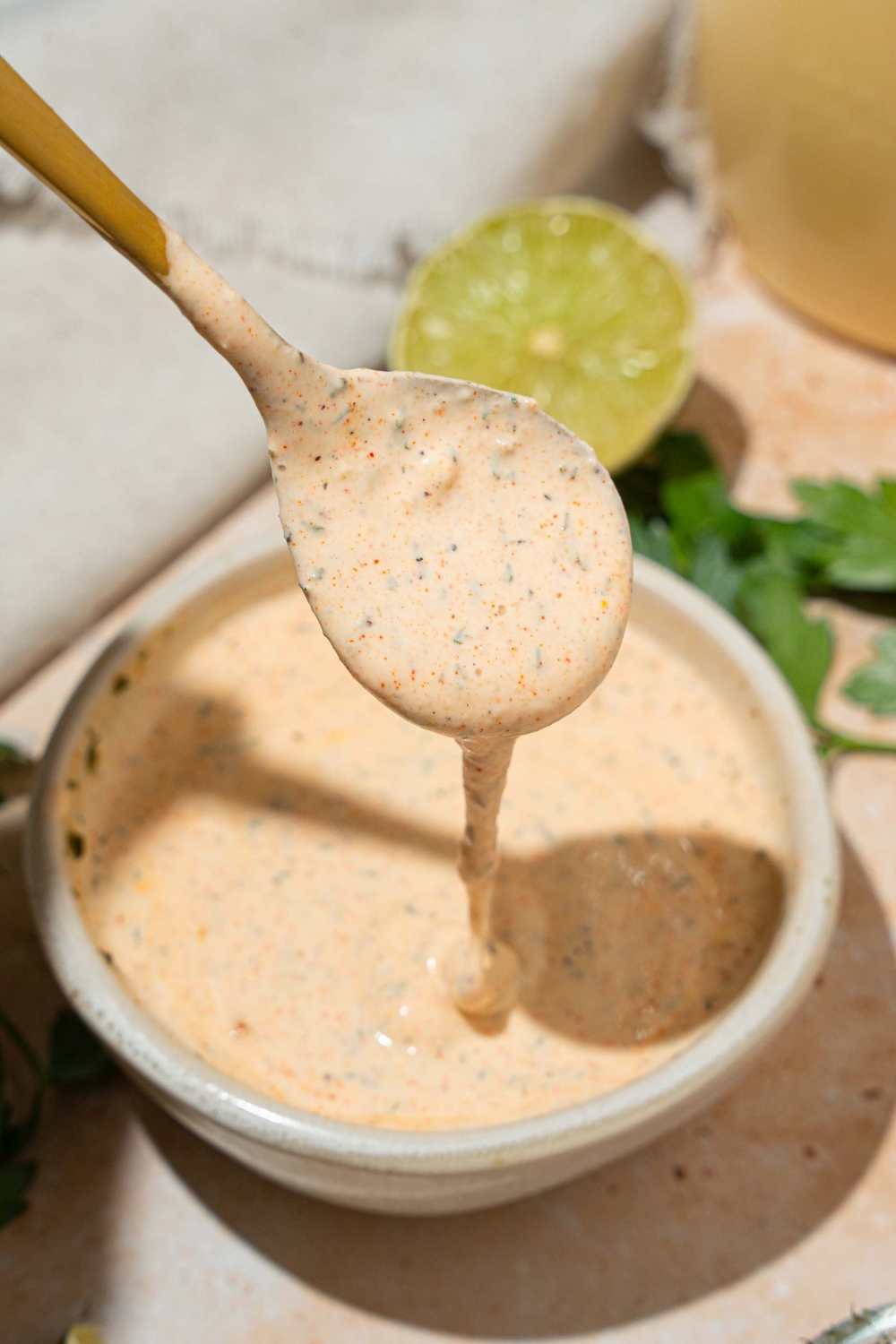 A white bowl with Popeyes blackened ranch. A spoon is dipped in the bowl. The bowl is on at tan counter with a lime.