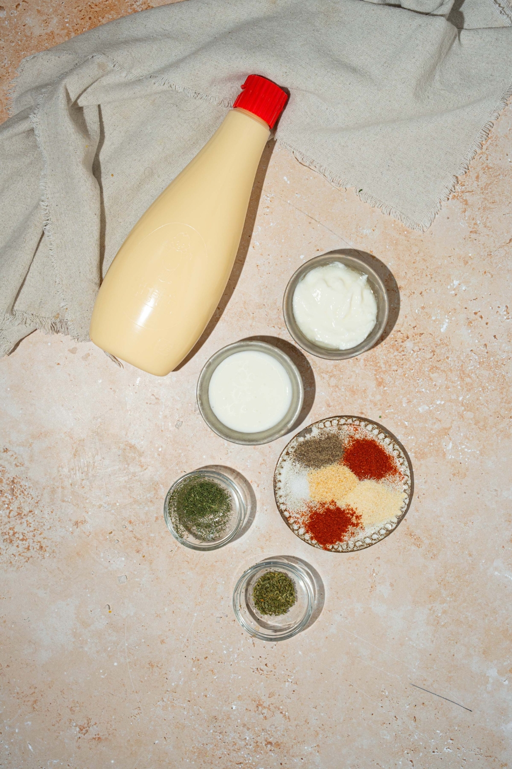 A tan counter with several bowls containing ingredients to make Popeyes blackened ranch including mayo, buttermilk, sour cream, and seasonings.