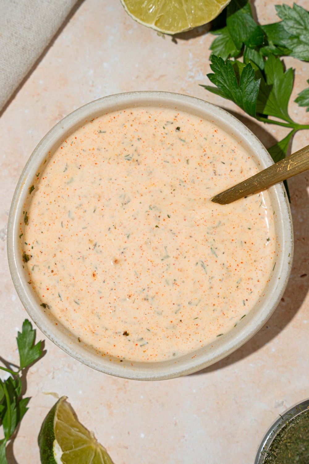 A white bowl with Popeyes blackened ranch. A spoon is in the bowl. The bowl is on at tan counter with a lime.