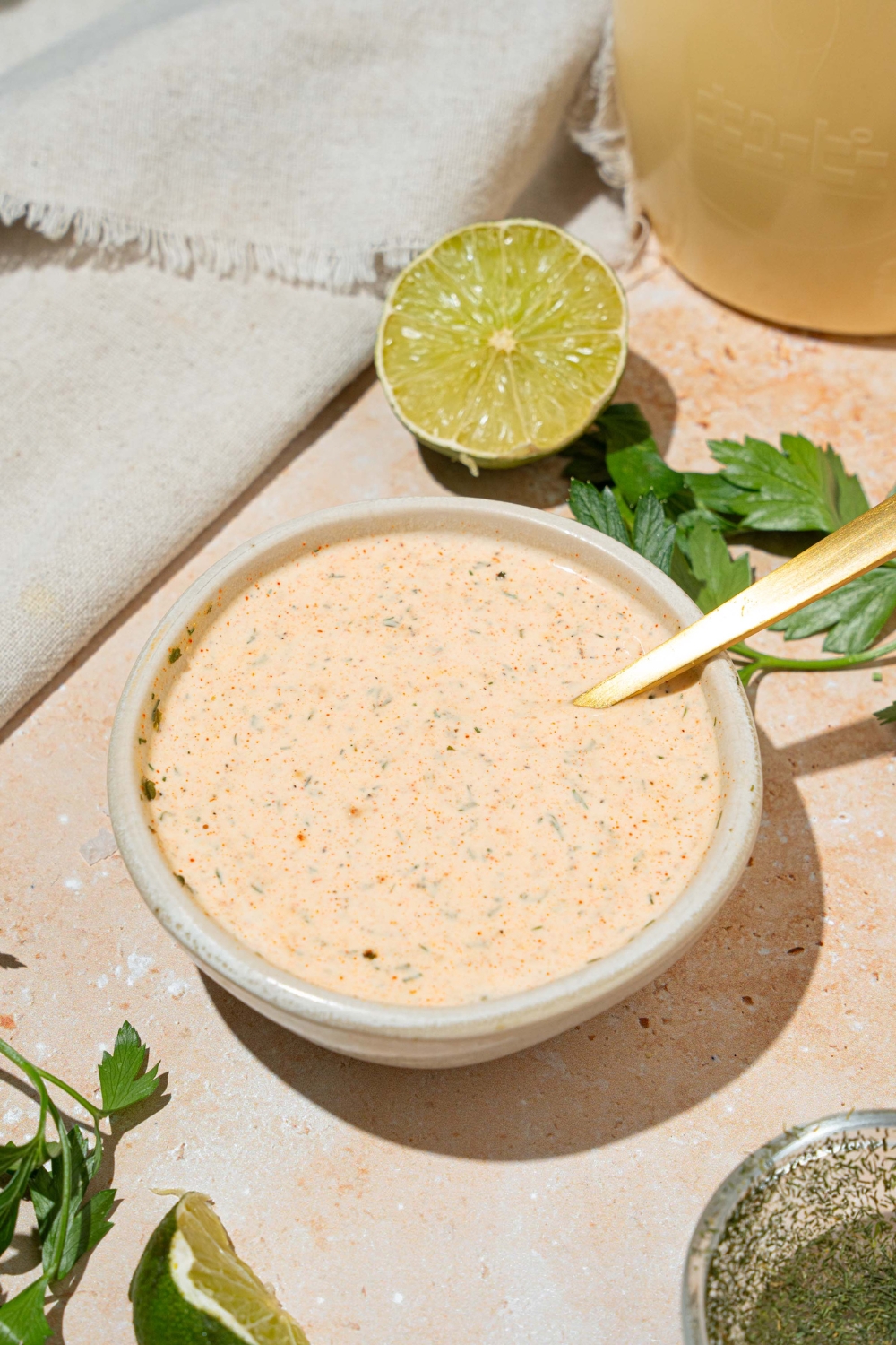 A white bowl with Popeyes blackened ranch. A spoon is in the bowl. The bowl is on at tan counter with a lime.