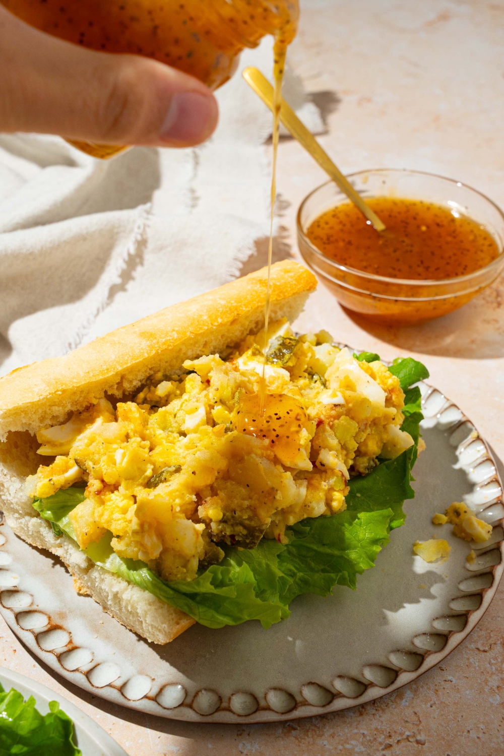 An open sandwich with sweet onion sauce being poured over the sandwich. The sandwich is on a tan counter with a bowl of sweet onion sauce and white cloth napkin.