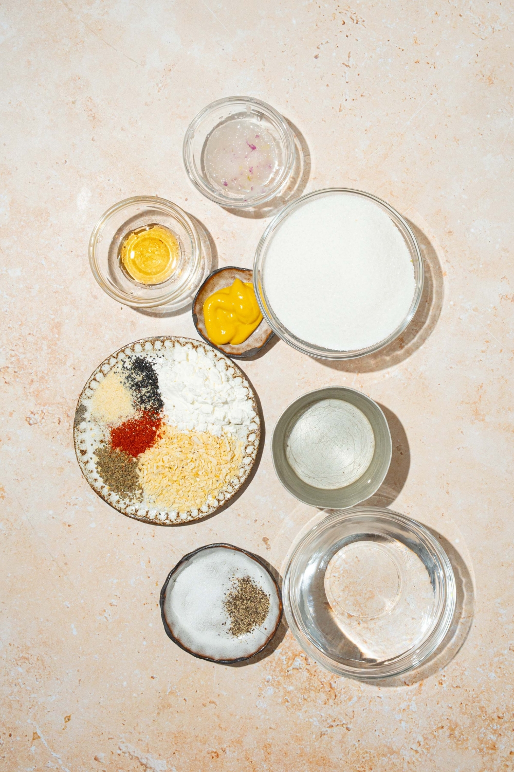 A tan counter with several bowls in various sizes containing ingredients to make sweet onion sauce including sugar, vinegar, onion, mustard, sesame oil, cornstarch, and seasonings.