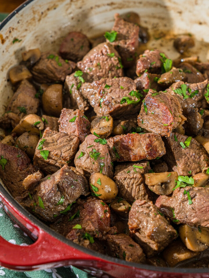 A cast iron skillet with tenderloin tips cooked with mushrooms and garnished with fresh parsley.