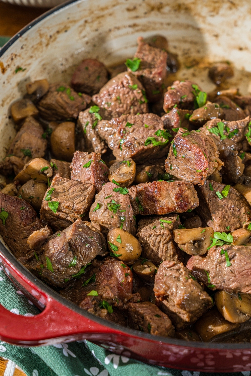 A cast iron skillet with tenderloin tips cooked with mushrooms and garnished with fresh parsley.