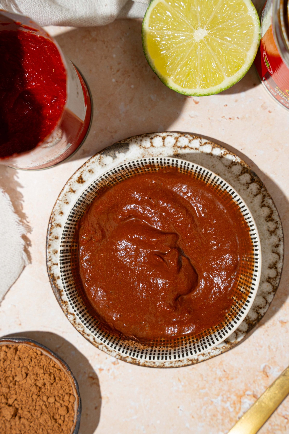 A white bowl of Tex Mex paste on a small plate. The plate is on a tan counter with a lime and cans of ingredients.