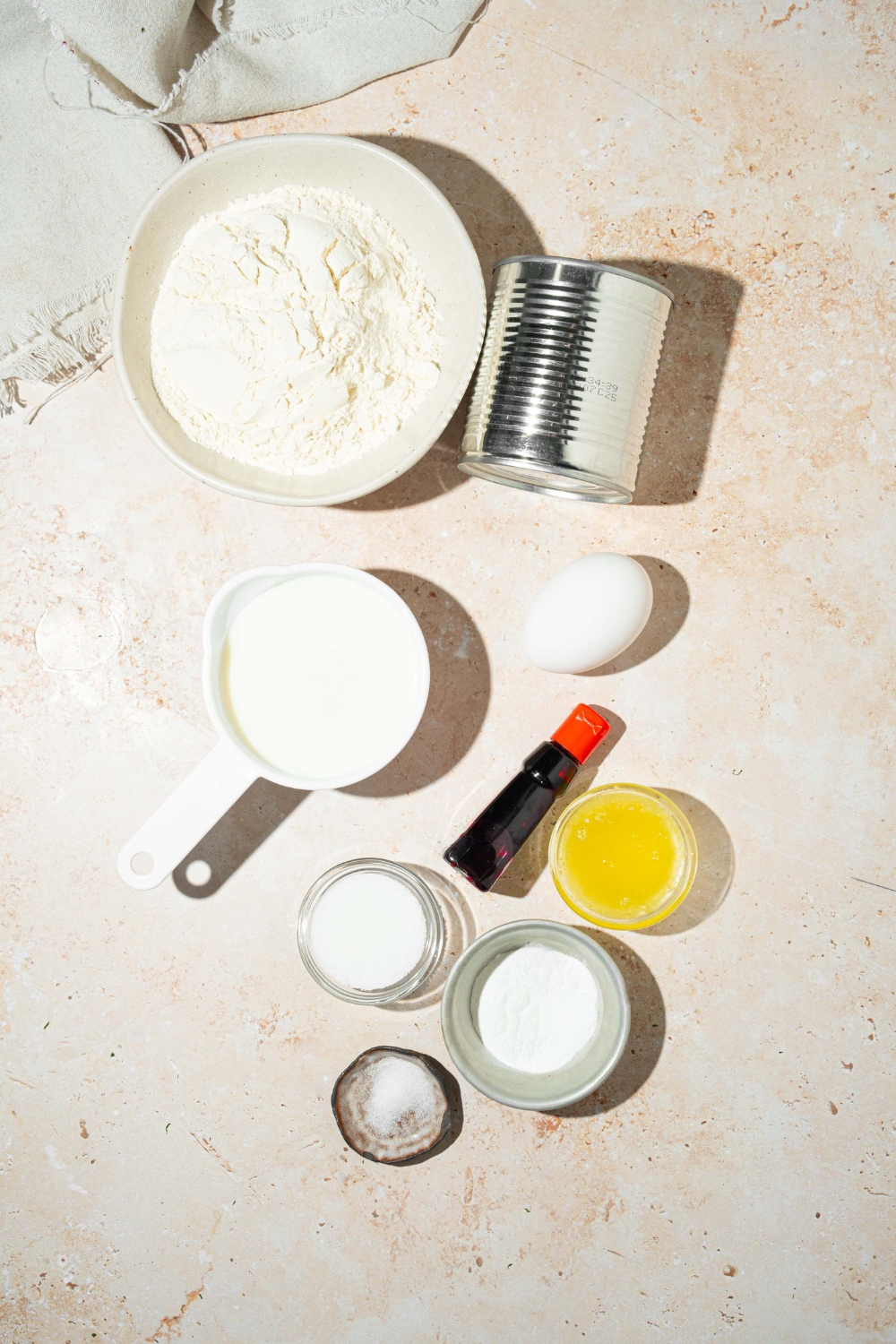 A tan counter with several bowls in various sizes containing ingredients to make ube pancakes including flour, coconut milk, condensed milk, sugar, baking powder, ube extract, egg, milk, and butter.