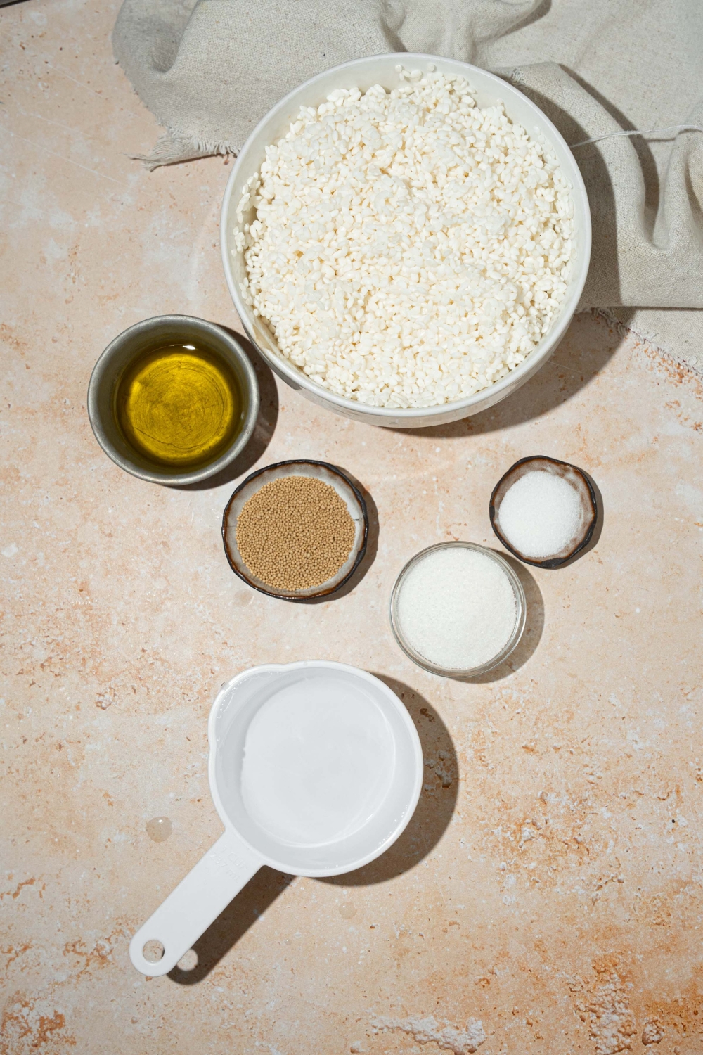 A tan counter with several bowls containing ingredients to make rice blender bread including soaked rice, honey, yeast, salt, water, and oil.