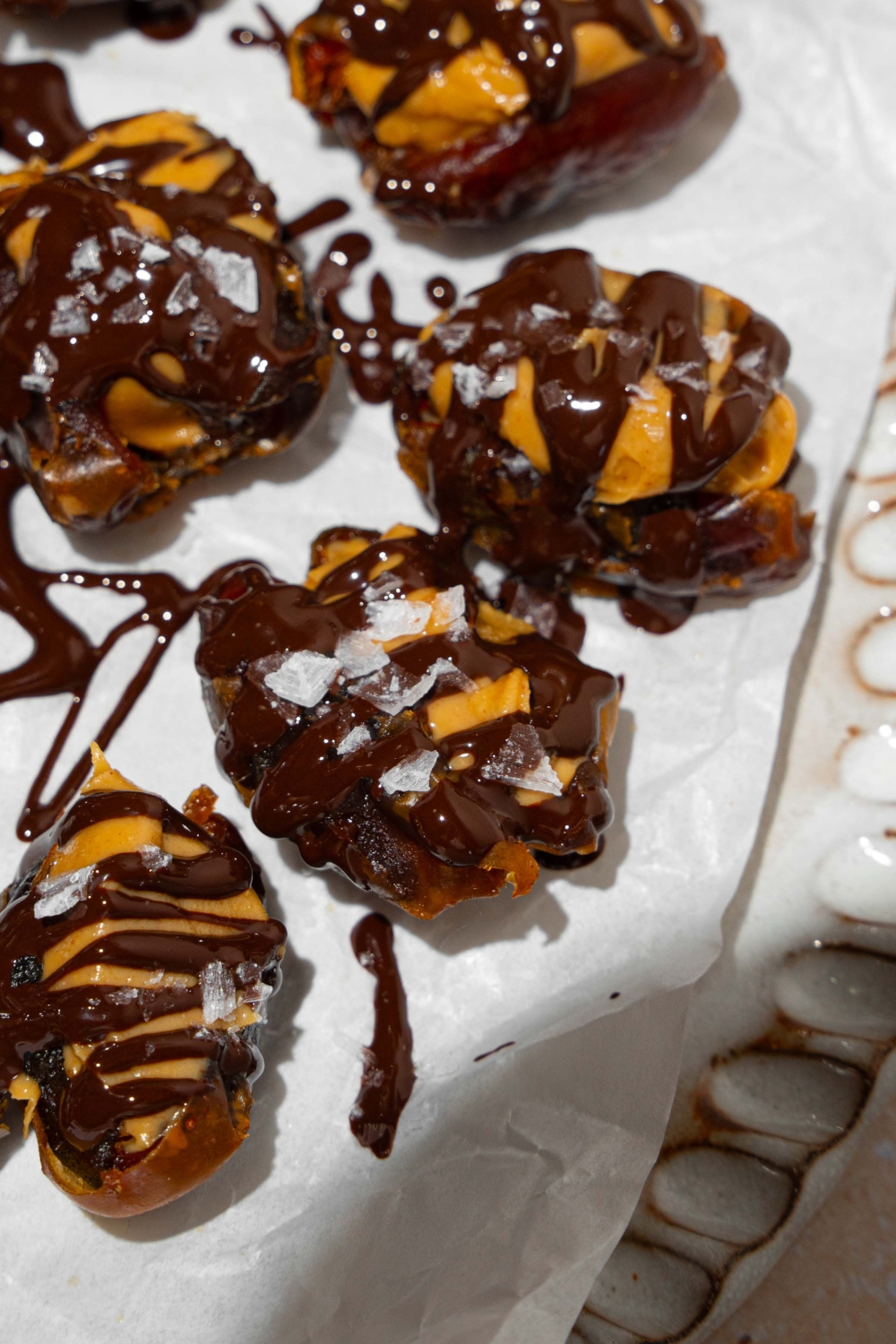 A plate lined with parchment paper with dates stuffed with peanut butter and drizzled with chocolate and sea salt.