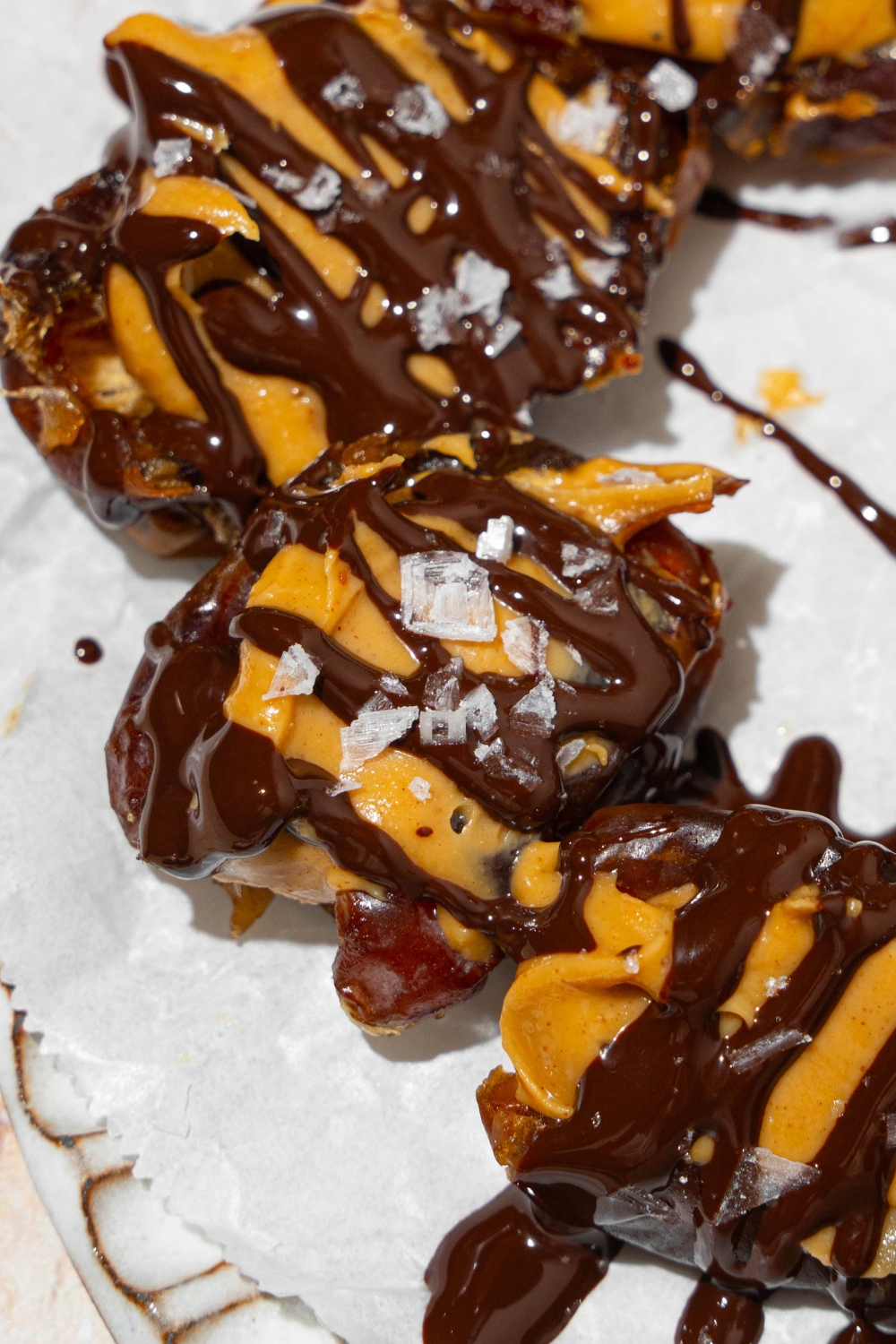 A plate lined with parchment paper with dates stuffed with peanut butter and drizzled with chocolate and sea salt.