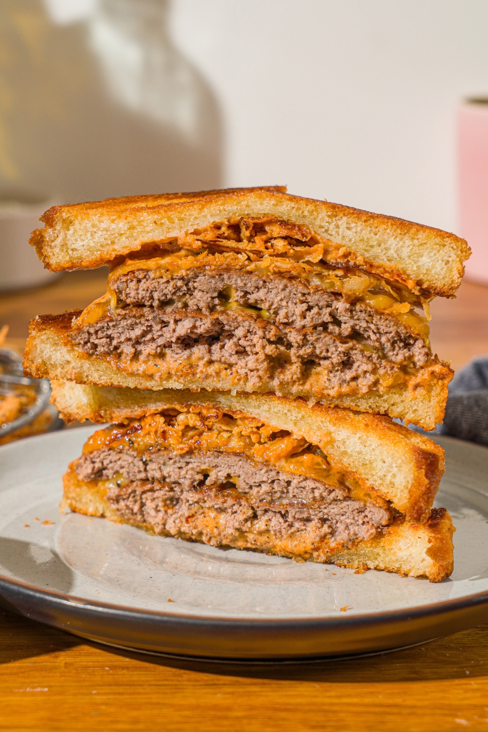A plate with a copycat Whataburger patty melt sliced in half and stacked on one another. The plate is on a wooden counter.